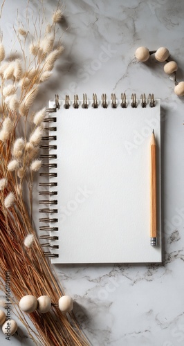 Blank spiral notepad with pencil, dried flowers, and beads on marble