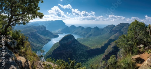 Panoramic view of a vast canyon, dramatic mountains, and a winding river under a vibrant sky