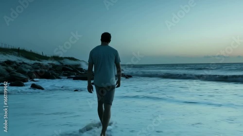 A serene video scene of a man walking along a rocky beach at sunset, captured from a low angle, highlighting the calm waves and twilight sky.