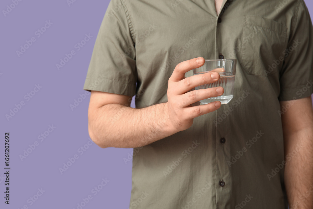 Fototapeta premium Young man with glass of clean water on lilac background
