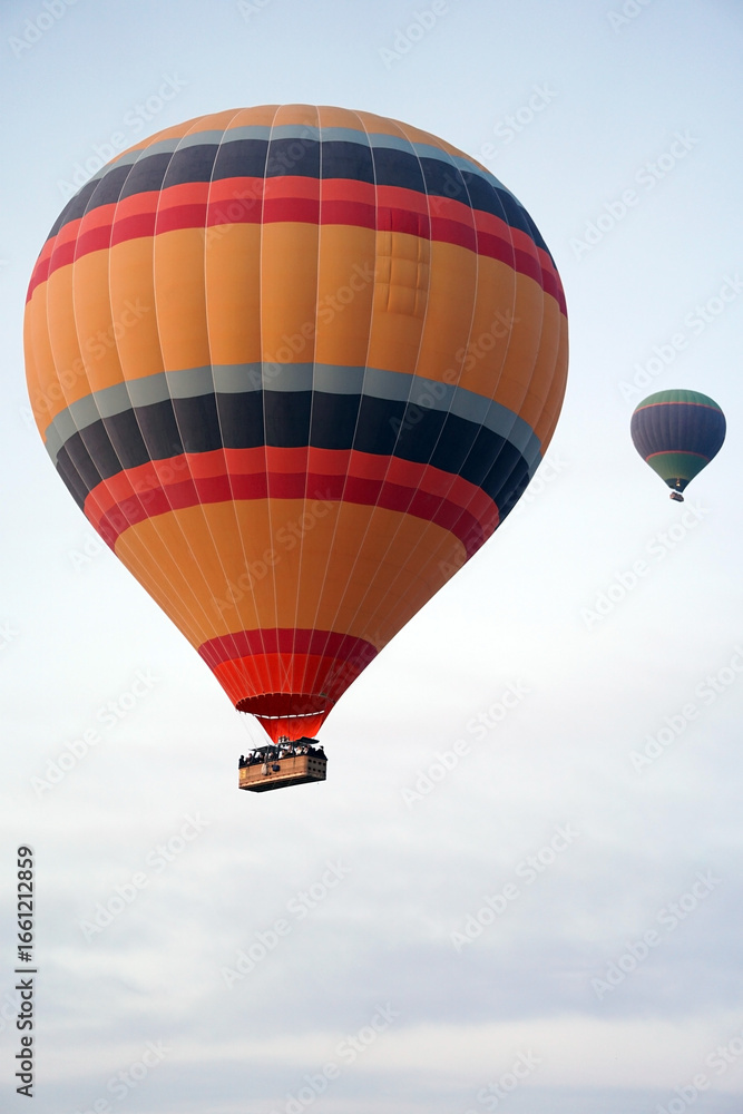 Fototapeta premium Colorful hot air balloons flying in the sky during sunrise, with passengers in the basket enjoying a scenic aerial adventure above the clouds