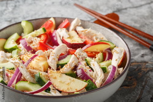 Asian salad with shredded chicken, cucumber, apple, red onion, bell pepper and sesame mustard dressing close-up in a bowl on the table. Horizontal