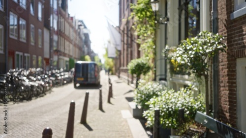 Photography Blurred city street in amsterdam showcases defocused bicycles, buildings, and foliage, capturing a sunny urban scene with van and pedestrians in the netherlands for a serene atmosphere