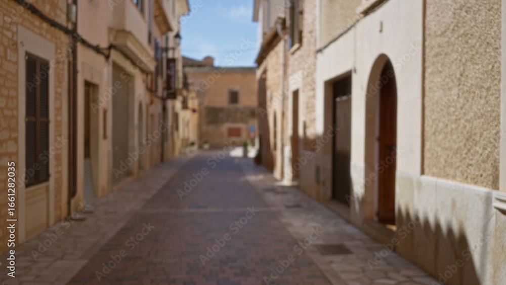 Fototapeta premium Blurred view of a quiet mediterranean old town street, with sunlit stone buildings and a distant bokeh effect, evoking a sense of serene urban wanderlust.