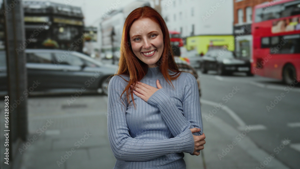 Fototapeta premium Woman smiling on city street with cars passing by, highlighted by vibrant red hair and casual outfit in urban outdoor setting suggesting british atmosphere.
