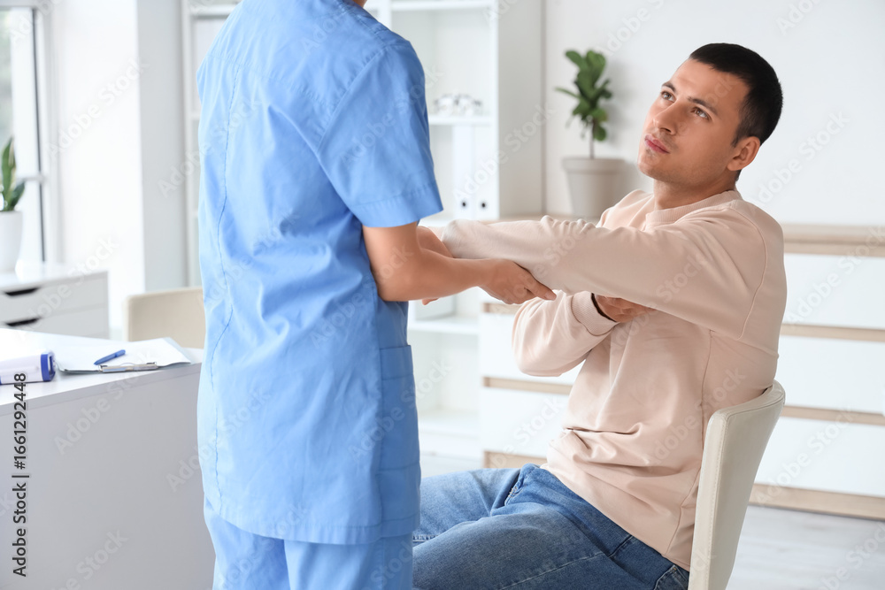 Obraz premium Young man with pain in his elbow visiting doctor at hospital