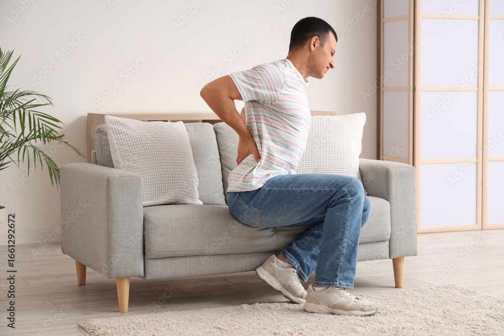 Fototapeta premium Young man suffering from back pain on sofa at home