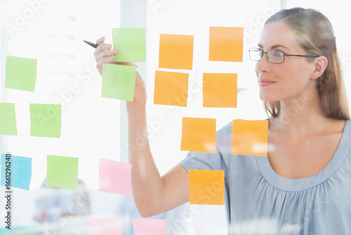 Mid adult female moving sticky note on glass board in meeting room with pen, copy space