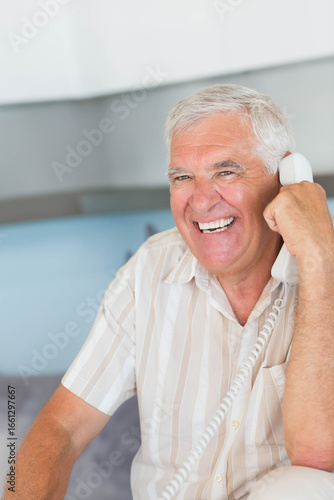 Smiling senior man holding corded telephone receiver and talking at home desk, copy space