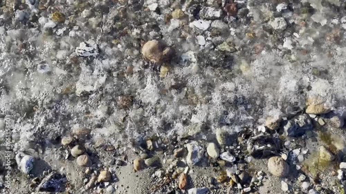 Gekräuselte Wasseroberfläche am steinigen Ufer des Comer See, mit leichten Wellen, von oben 