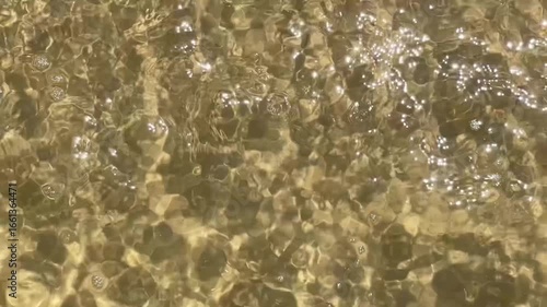 Gekräuselte Wasseroberfläche am Strand mit Lichtreflexen und leichten Wellen, von oben 