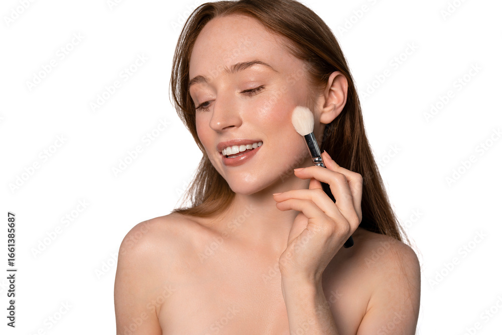 Young woman applying blush with a brush while smiling, showcasing a natural beauty look in a well-lit studio setting Young woman applying blush with a brush while smiling, showcasing a natural beauty look in a well-lit studio setting