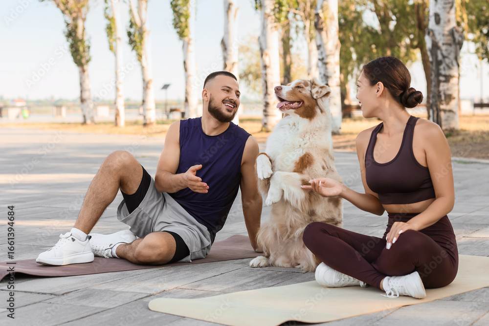 Sporty young couple with Australian Shepherd dog on fitness mats outdoors Sporty young couple with Australian Shepherd dog on fitness mats outdoors