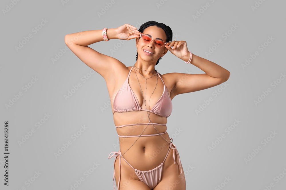 Fototapeta premium Pretty young African-American woman in bikini with accessories and sunglasses on white background