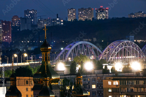Fényképezés Golden domes and illuminated arched bridges against a dynamic city skyline at twilight in Kyiv, Ukraine