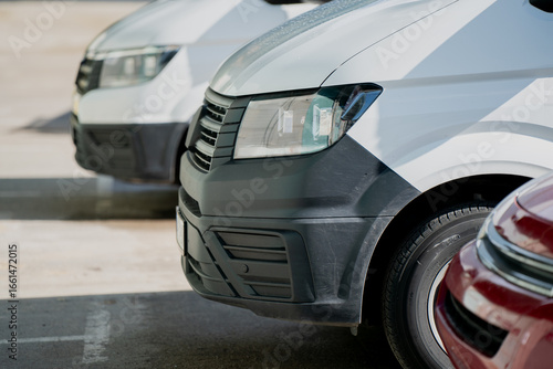 Commercial vehicles parked in line, close view of van fronts with bumper and light detail, modern automotive fleet for transport, delivery services, logistics operations, company vehicles on site