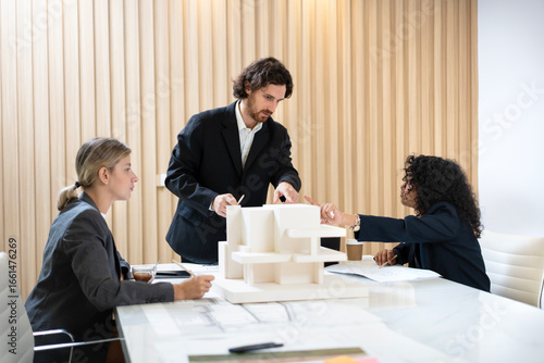 Businessman leading a meeting and presenting a housing project plan using a scale model to his colleagues in a modern office