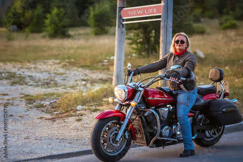 Mature woman on a red motorcycle passing a road sign with message “New Life”, symbolizing change, freedom, courage and new beginnings in midlife journey
