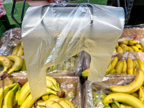 Plastic produce bag hanging above fresh bananas in a grocery store highlights issues of food packaging, consumer waste, and environmental sustainability
