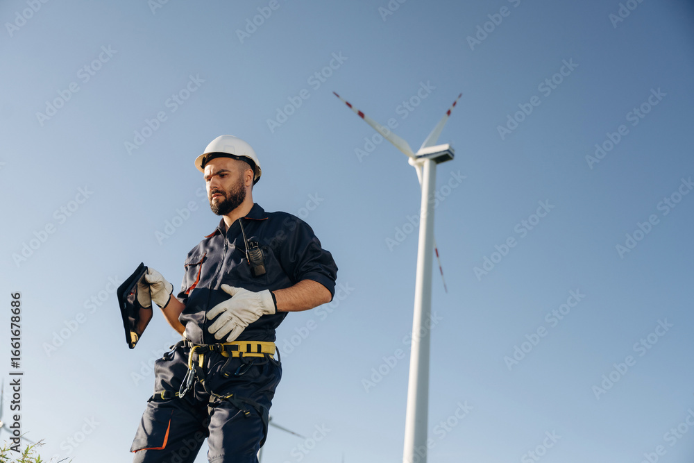 Naklejka premium Against blue sky. Engineer in field checking on wind turbine production