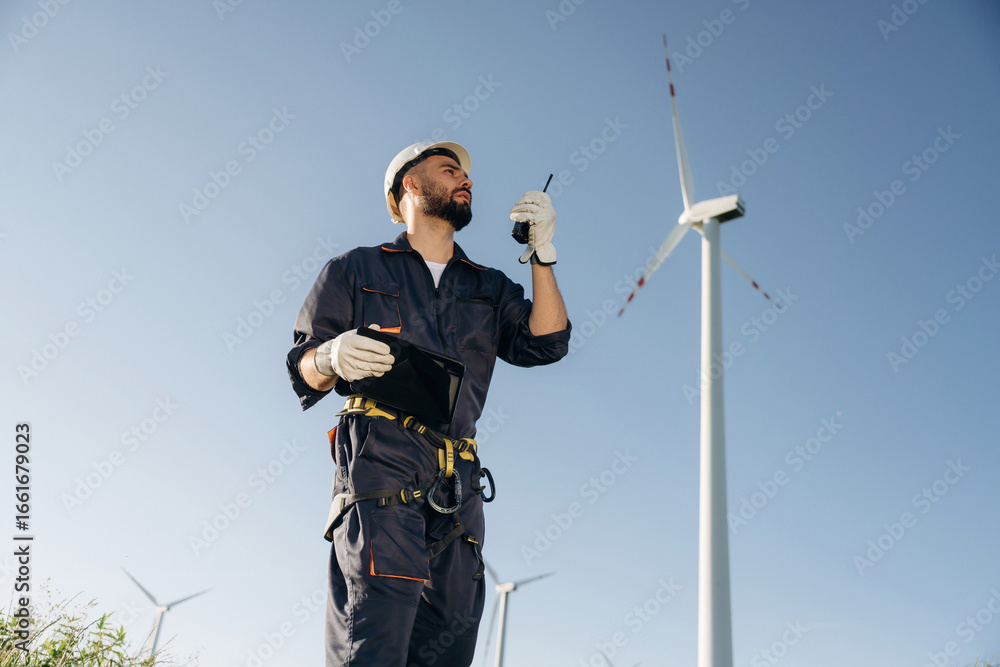 Naklejka premium Giving orders by using walkie talkie. Engineer in field checking on wind turbine production