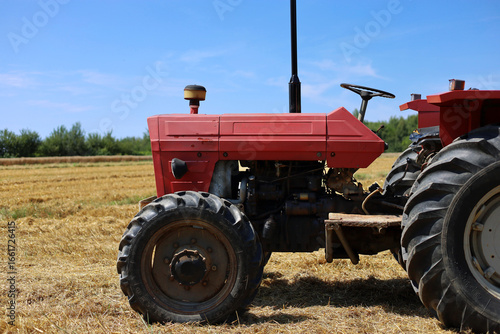 Side view of an old, red tractor with visible engine parked on the mowed wheat field