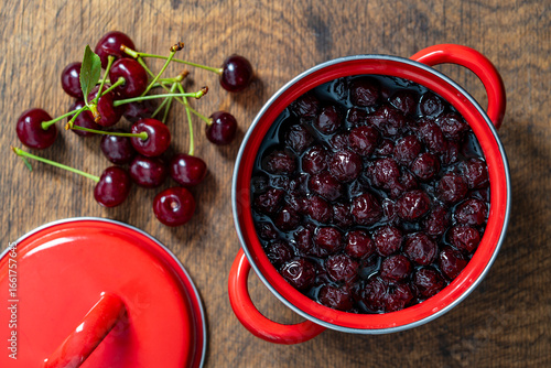 Delicious cherry jam in a red saucepan on a wooden table, closeup, top view. Summer preparation and preservation of berries for the winter, home cooking