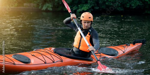 Foto Man in a helmet and life jacket paddles an orange kayak on a calm river