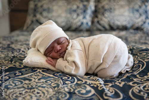 Dark skinned newborn baby sleeping on bed with white blanket and small pillow and white beanie