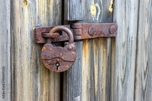 Rusty old padlock on wooden door, vintage security and rustic architectural detail.