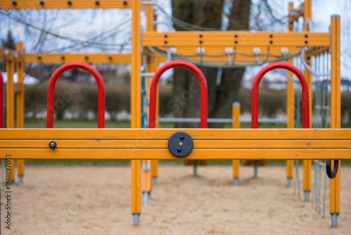 Modern playground climbing structure with red and yellow bars, outdoor play equipment for children.