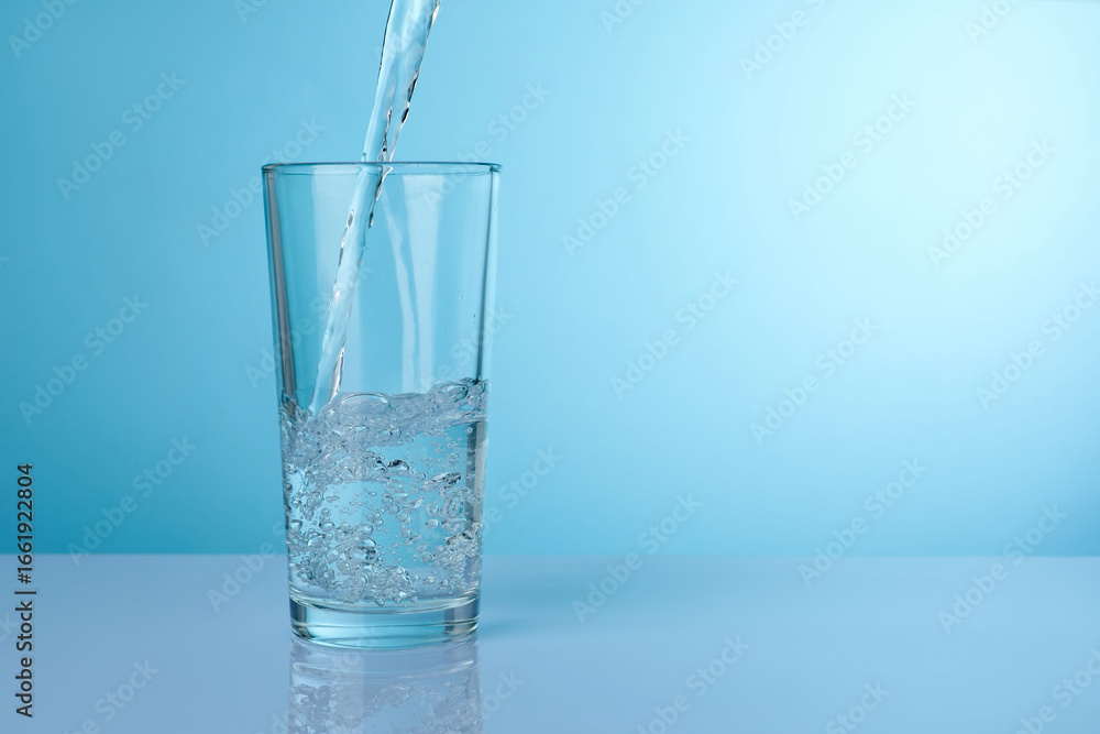 Pouring refreshing soda water into glass at light grey mirror table against turquoise gradient background, closeup. Space for text Pouring refreshing soda water into glass at light grey mirror table against turquoise gradient background, closeup. Space for text