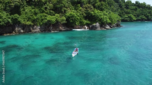 A fishing boat floats on turquoise waters off Pulau Nasi, Sumatra, Indonesia. The drone pulls back and ascends, unveiling the lush green coastline and the vibrant tropical sea.
