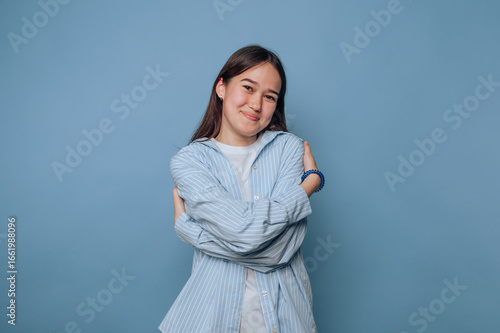 Young woman in casual clothing hugging herself against blue background.