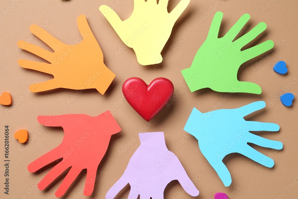 Obraz premium Tolerance concept. Colorful paper hands and hearts on brown background, flat lay