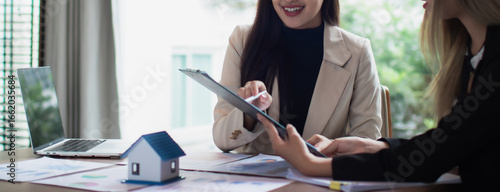 Asian female real estate businesswoman in suit smiling while advising clients on insurance, trusts, finance and successful contract agreements.