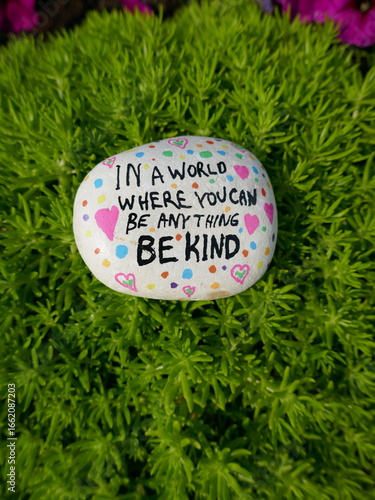 In a world where you can be anything be kind kindness rock on green moss vertical photo
