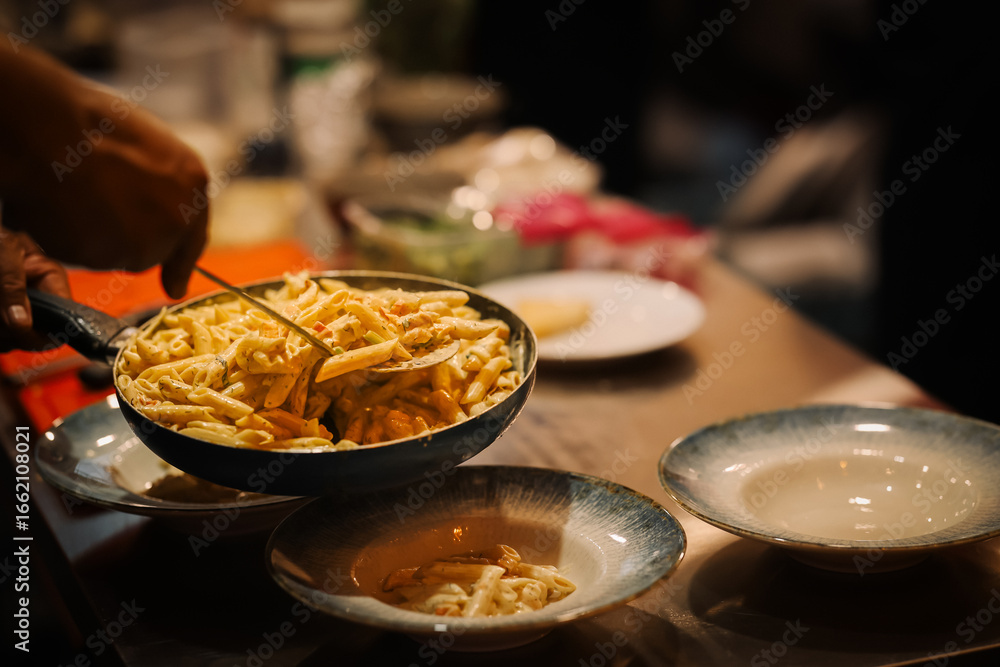 Chef serving creamy penne pasta with herbs and vegetables into elegant ceramic plates, capturing the warm atmosphere of a busy professional kitchen Chef serving creamy penne pasta with herbs and vegetables into elegant ceramic plates, capturing the warm atmosphere of a busy professional kitchen