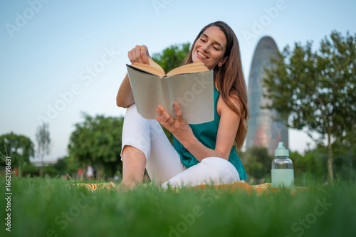 Photography Young woman reading a book in a park in barcelona near torre glòries
