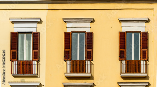 old yellow facade of house with three brown vintage wooden windows in retro italian european style