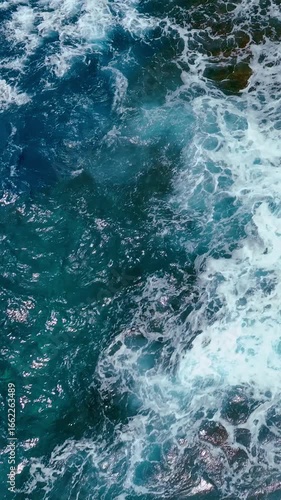 Ocean water background with foam. Pacific ocean water splash. Rocky bottom in the water. Aerial top view. Vertical video.