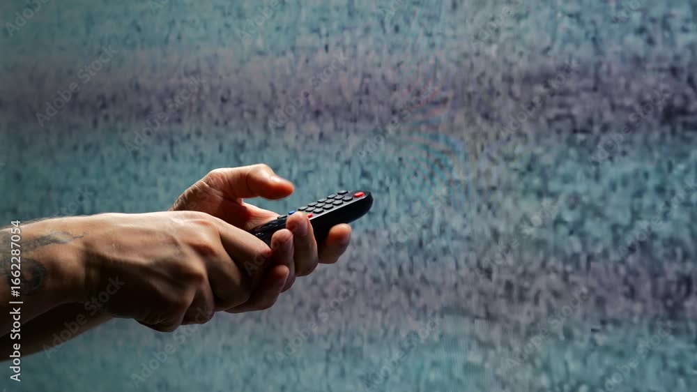 Hand with remote control in front of non-working TV showing white noise ...