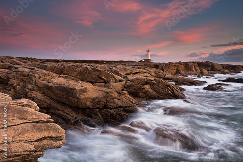 Ploemeur Morbihan Waves crashing against rocky coast at sunset with vibrant pink and orange skies.