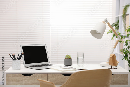 Stylish workplace with laptop and stationery on white table in office