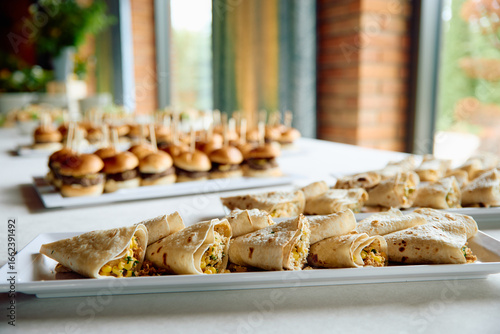 Appetizer wraps and mini burgers on trays at event