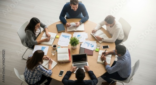 Overhead view of a business meeting with people around a table with laptops and documents spread out