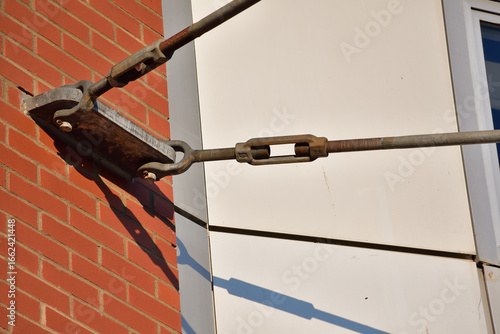 Turnbuckle and threaded rods tensioning device attached to brick wall anchor point.