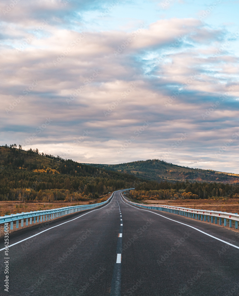 Fototapeta premium A long, open highway leads through a picturesque mountainous area.