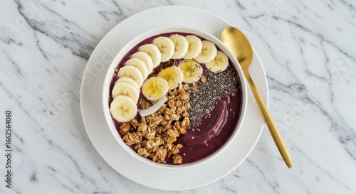 Açaí bowl with banana slices, granola, and chia seeds on a white plate with a gold spoon
