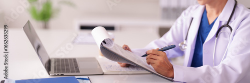 Asian adult female doctor physician medical professional documents patient chart notes healthcare provider uses laptop computer clinic office setting